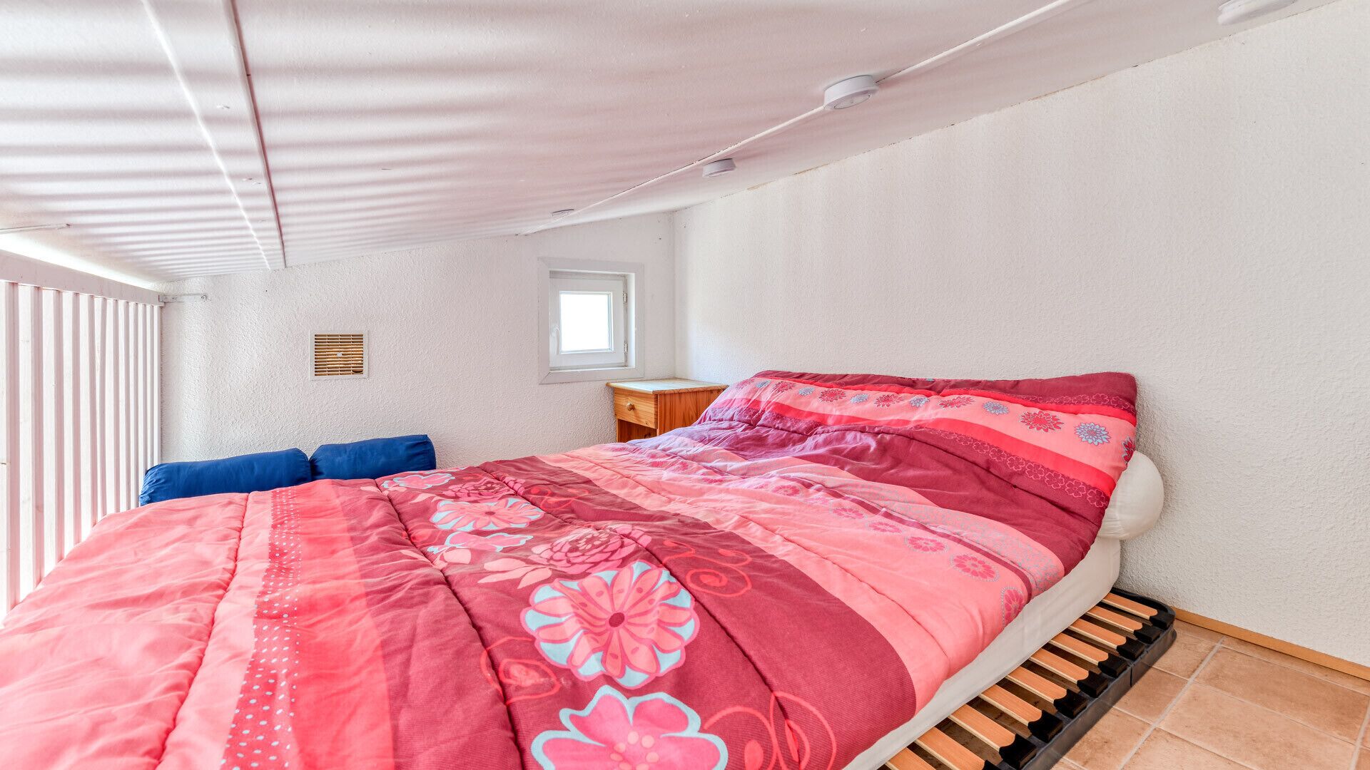 Ein Schlafzimmer mit Bett, Fenster, Nachttisch und Heizkörper.