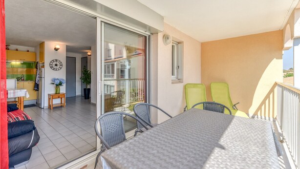 A balcony with a table and chairs, a sliding glass door leading to a kitchen, and a clock on the wall. - Modern apt 4 ppl, equipped loggia, pool (Agde)