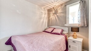 A bedroom with a bed, a nightstand, a lamp, and a window with curtains. - Modern apt 4 ppl, equipped loggia, pool (Agde)