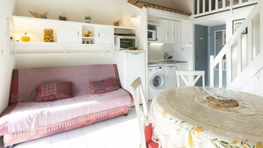 A cozy living area with a sofa, a dining table with a decorative bowl, a washing machine, and a kitchen with white cabinets and a microwave. - Tiny house 4/6 ppl, terrace, private parking (Agde)