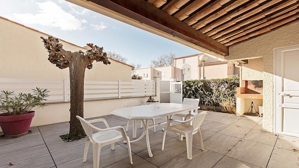 Une terrasse couverte avec une table et des chaises, un arbre et une clôture blanche.