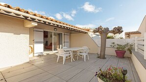 Une terrasse avec une table et des chaises, un pot de fleurs et un arbre.