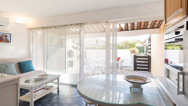 A modern kitchen with a glass table, white cabinetry, and a view of the backyard. - Apt 4 ppl, terrace, private parking (Agde)