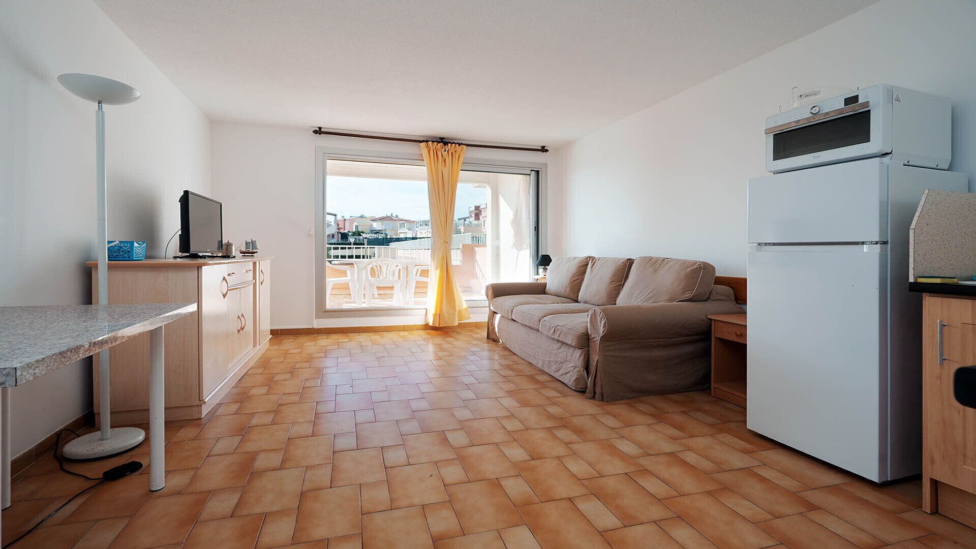 A compact living space with a kitchenette, a sofa, a dining area, and a view through a window with curtains.