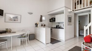 Een compacte keuken met witte kastjes, een eethoek met tafel en stoelen, en een trap naar een verdieping erboven.