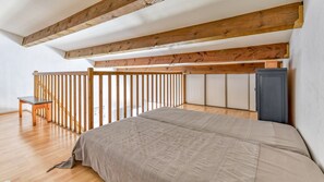 Quarto com cama, vigas de madeira no teto, escrivaninha e guarda-roupa.