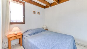 Une chambre à coucher avec un lit, une table de chevet, une lampe, une fenêtre et un tableau au mur.