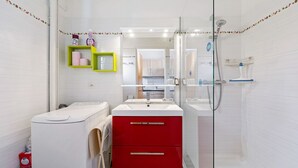Un bagno moderno con una lavatrice bianca, un armadietto rosso, un box doccia in vetro e uno specchio che riflette una zona cucina.