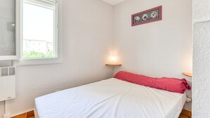 A bedroom with a bed, a window, a wall-mounted picture, and a wall-mounted light fixture. - Bright apt 4/6 ppl, terrace, free parking (Agde)