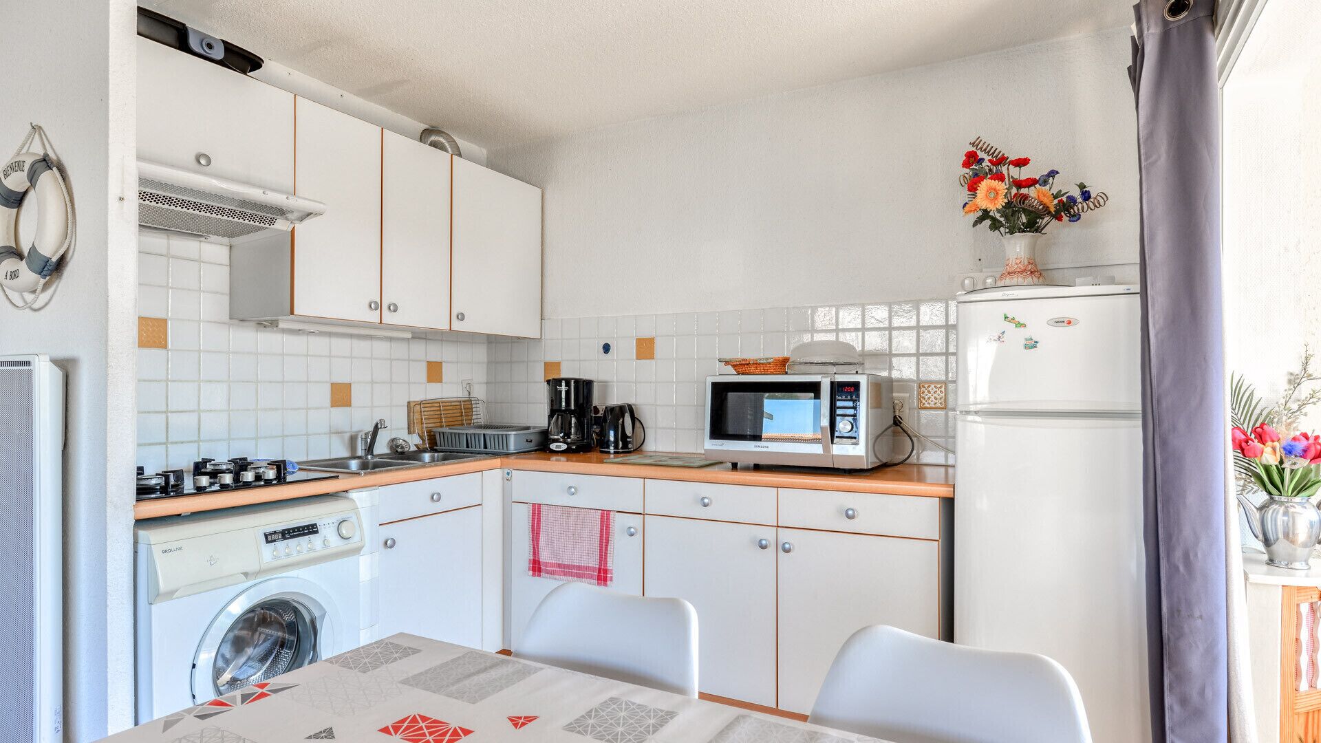 Una cucina compatta con lavatrice, forno a microonde e un tavolo con sedie.