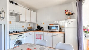 A compact kitchen with a washing machine, microwave, and a table with chairs. - Bright apt 4/6 ppl, terrace, free parking (Agde)