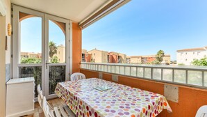 Een balkon met een tafel, stoelen en uitzicht op omliggende gebouwen.