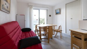 A room with a red sofa, a wooden table with chairs, a radiator, and a door leading to a balcony.