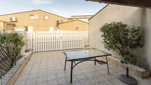 Un patio con una mesa de vidrio, una cerca blanca y un edificio al fondo.