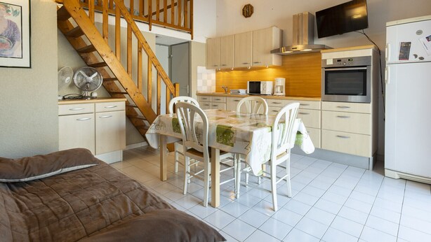 A compact kitchen with a dining table, wooden staircase, and a bed in the foreground. - Duplex house 4/6 ppl, terrace, near the sea (Agde)