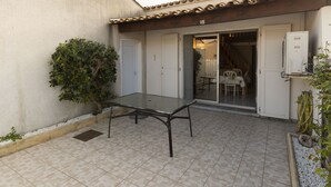 A patio with a glass table, a potted plant, and a building entrance with a door and a window. - Duplex house 4/6 ppl, terrace, near the sea (Agde)