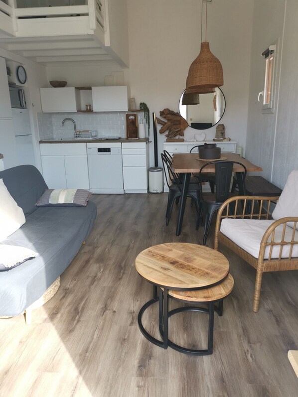 A compact living space with a kitchenette, a dining area with a round wooden table, and a sofa.