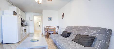 A compact living space with a kitchenette, a dining area, and a sofa with a patterned cover.