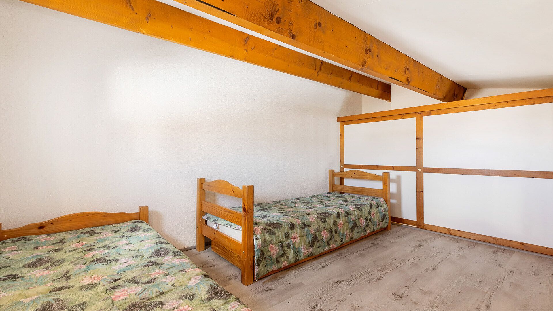 Ein Zimmer mit zwei Holzbettständern, einem Holzbalken an der Decke und einer schlichten weißen Wand.