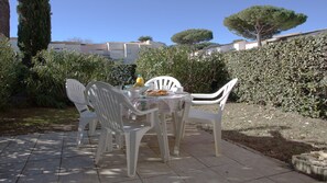 Patio esterno con sedie e tavolo in plastica bianca apparecchiati per la colazione.