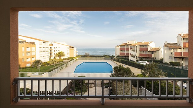 A view of a swimming pool with a clear sky and ocean in the background.