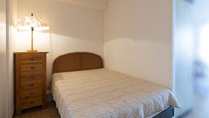 A small, single-bed room with a wooden headboard, a wooden dresser with drawers, and a lamp on the dresser.