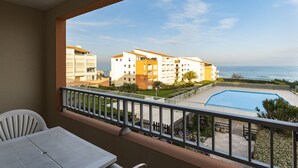 A balcony with a view of a swimming pool, adjacent buildings, and the ocean.