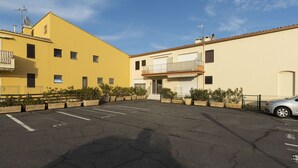 A parking lot with a yellow building and a beige building with a balcony.