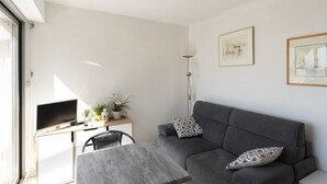 Una sala de estar moderna con un sofá gris, una mesita, un televisor y un escritorio con una computadora y elementos decorativos.