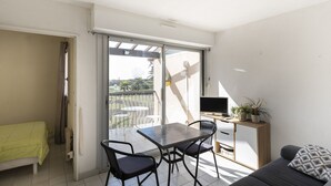 Un balcón con una mesa, sillas, un sofá y un televisor sobre un mueble de madera.