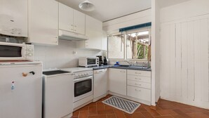 Cocina compacta con armarios blancos, microondas, estufa, tostadora y cafetera.