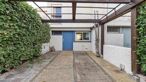 Un estrecho callejón con una puerta azul, una pared blanca y una estructura de pérgola de madera.