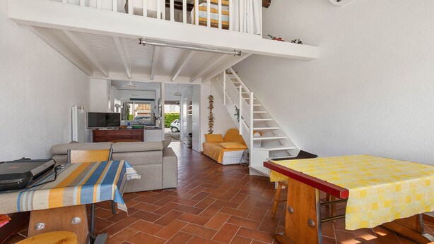 Un espacio habitable compacto con un dormitorio entre pisos, una zona de comedor y un rincón americano.