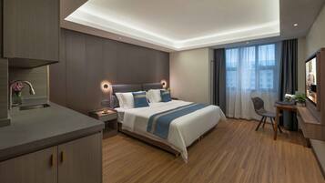 Una habitación de hotel moderna con una cama grande, un escritorio, una silla y una kitchenette pequeña.