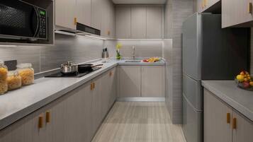 A modern kitchen with grey cabinetry, a stainless steel refrigerator, a microwave, and a sink with a vase of flowers.