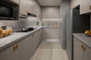 A modern kitchen with grey cabinetry, a stainless steel refrigerator, a microwave, and a sink with a vase of flowers. - Citadines Zhengda Mall Hefei (Hefei)