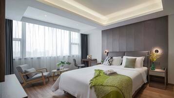 A modern hotel room with a large bed, a desk, a chair, and a small table.
