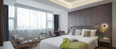 Quarto de hotel moderno com uma cama grande, uma escrivaninha, uma cadeira e uma mesa pequena.