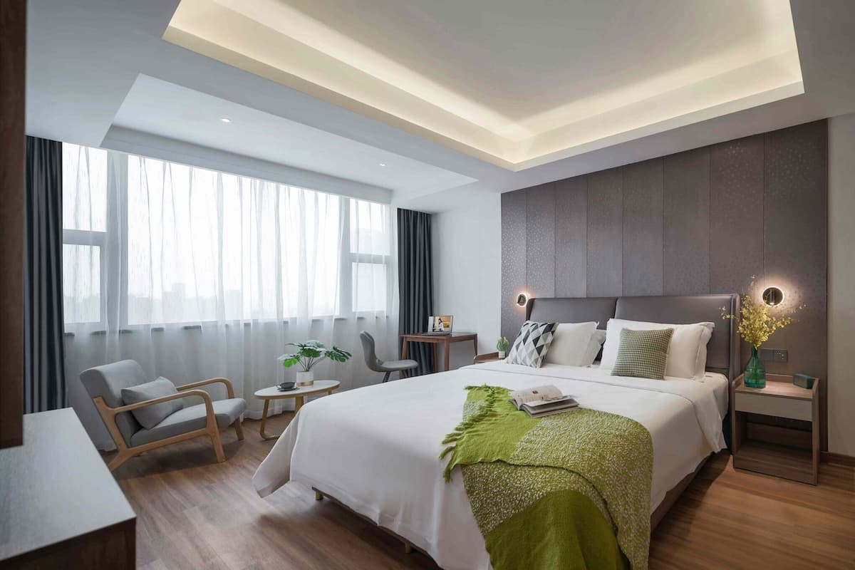 A modern hotel room with a large bed, a desk, a chair, and a small table.