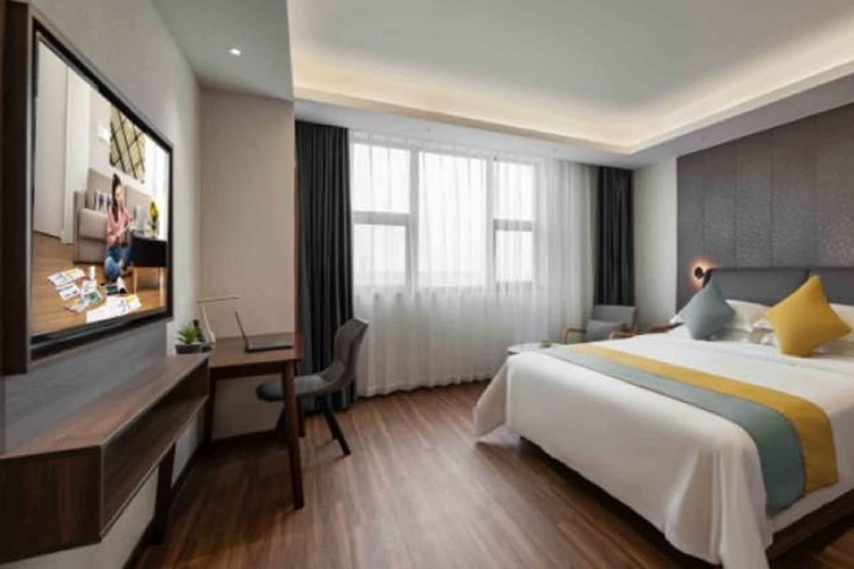 A modern hotel room with a large bed, a desk, a TV, and a window with curtains.