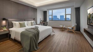 A modern hotel room with a large bed, a desk, a chair, a TV, and a city view.