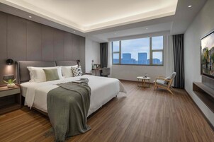 Habitación de hotel moderna con una cama grande, un escritorio, una silla, un televisor y vistas a la ciudad.