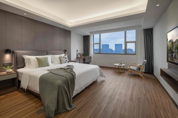 Habitación de hotel moderna con una cama grande, un escritorio, una silla, un televisor y vistas a la ciudad.