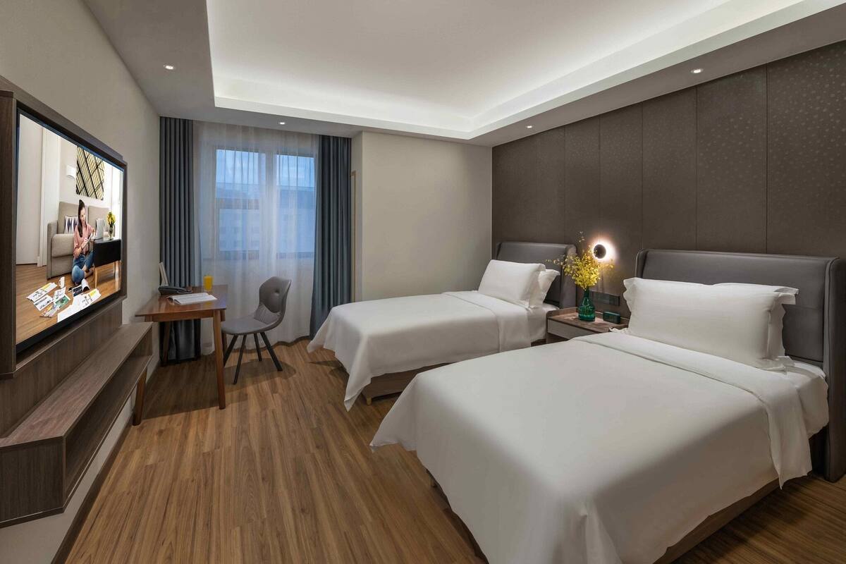 A hotel room with two beds, a desk, a chair, a TV, and a window with curtains.
