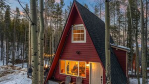 A red cabin with a large window and a door, surrounded by trees. - *NEW* Hidden Ruby A-Frame (Evergreen)