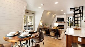 A modern loft-style living space with a dining area, kitchen, and a staircase. - *NEW* Hidden Ruby A-Frame (Evergreen)