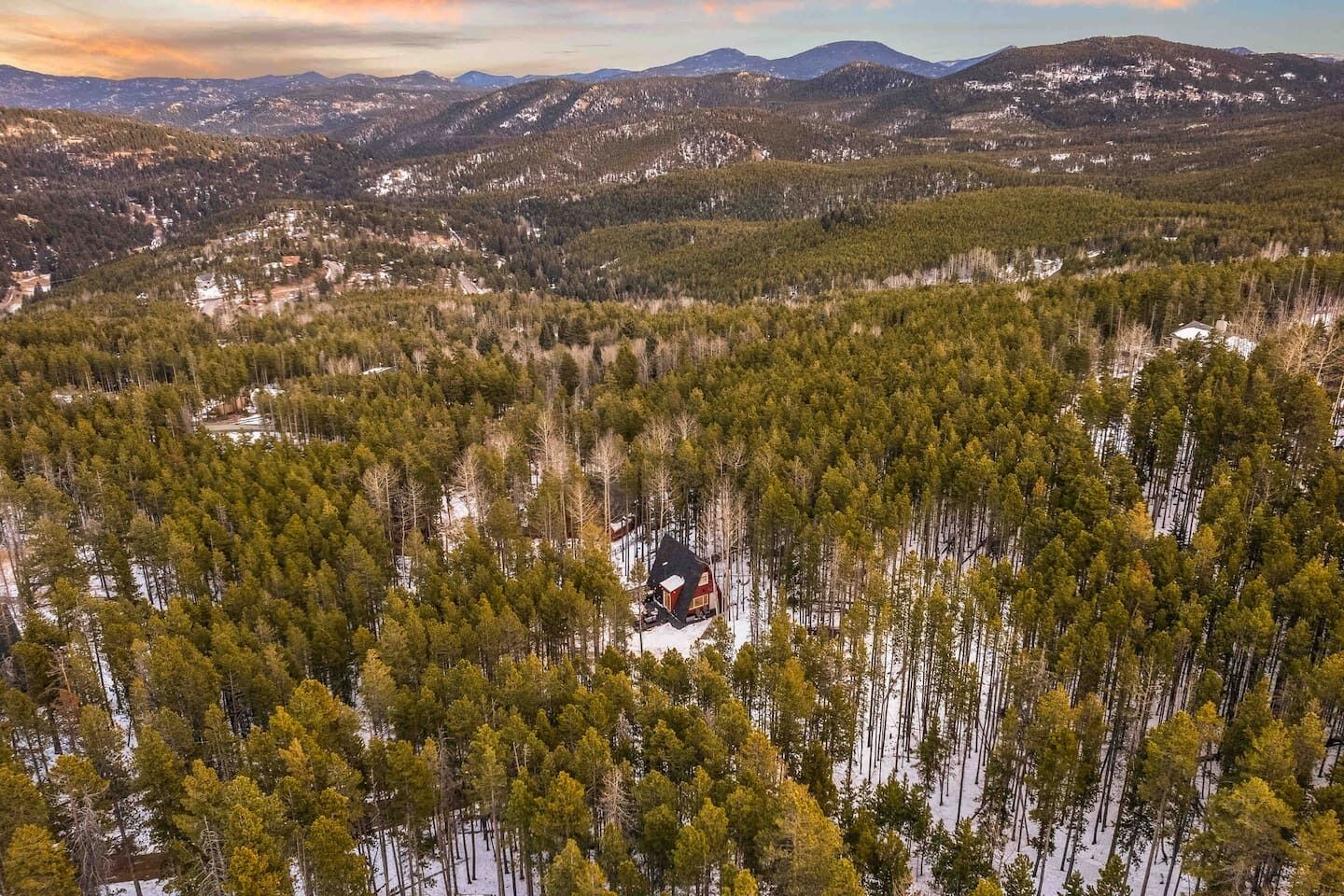 A remote cabin surrounded by dense forest and snow-covered terrain.