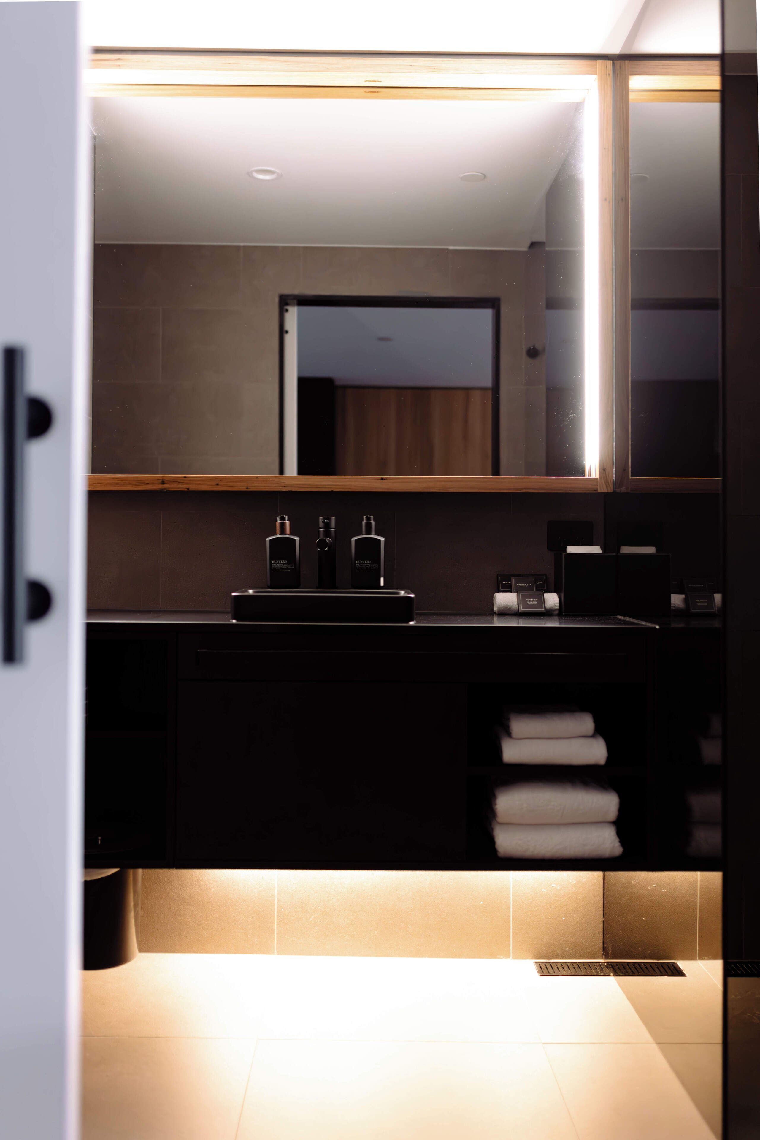 A modern bathroom with a large mirror, dark cabinetry, and a towel rack.