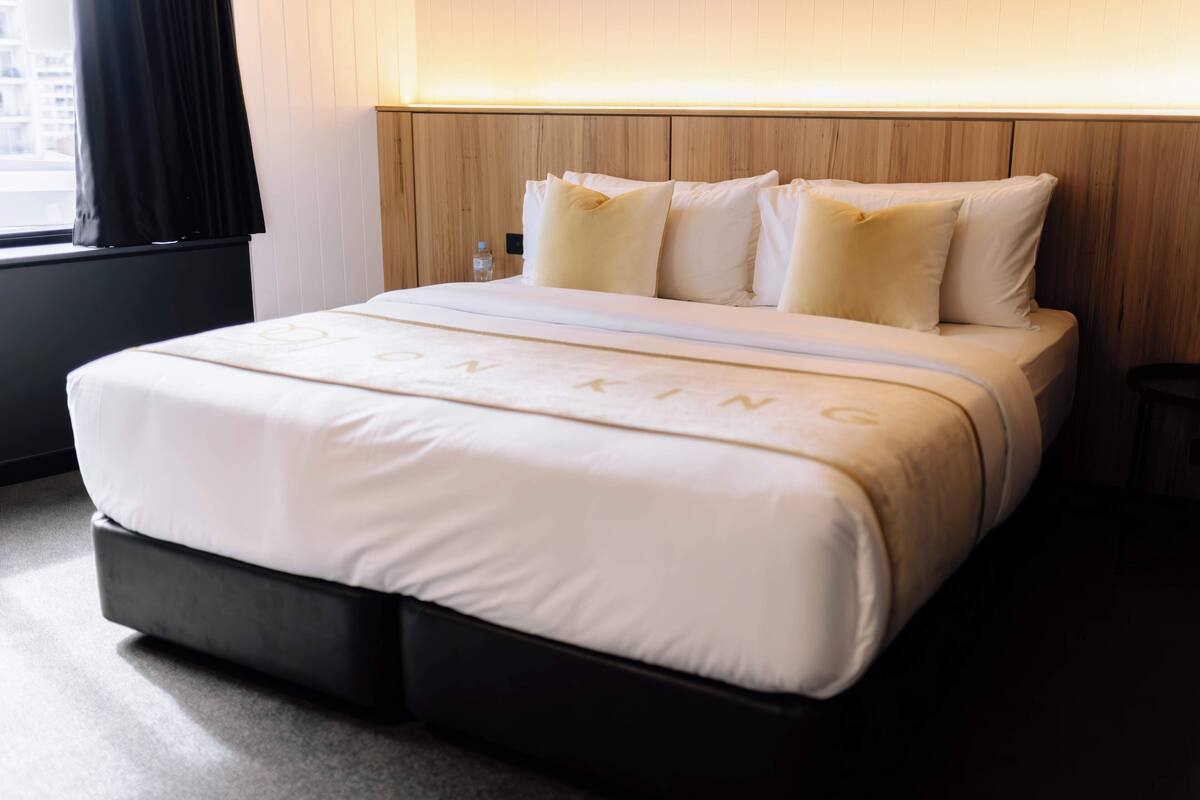 A neatly made bed with a white bedspread and pillows, a wooden headboard, and a small bedside table with a bottle.