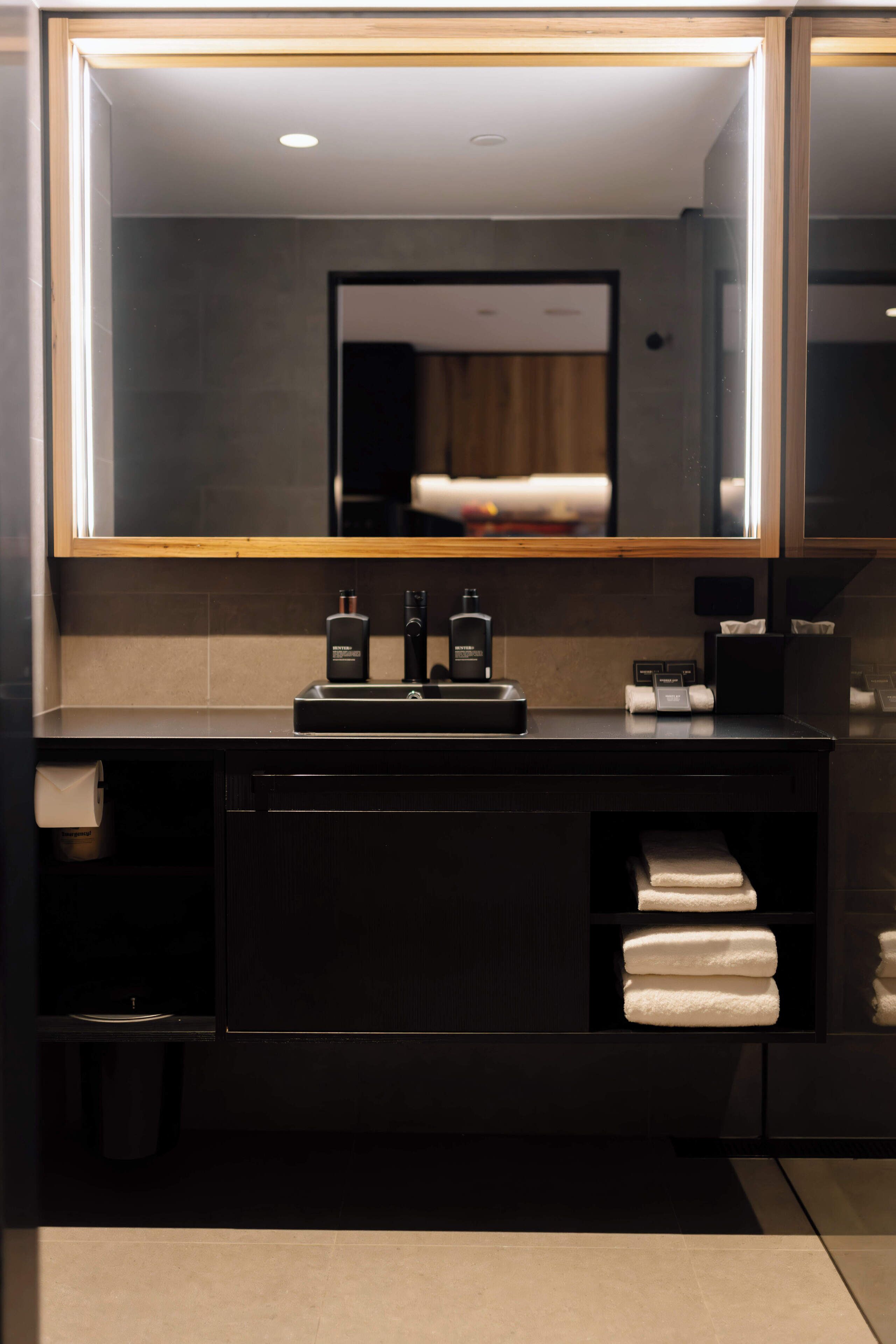 A modern bathroom with a large mirror, dark cabinetry, and neatly folded towels.
